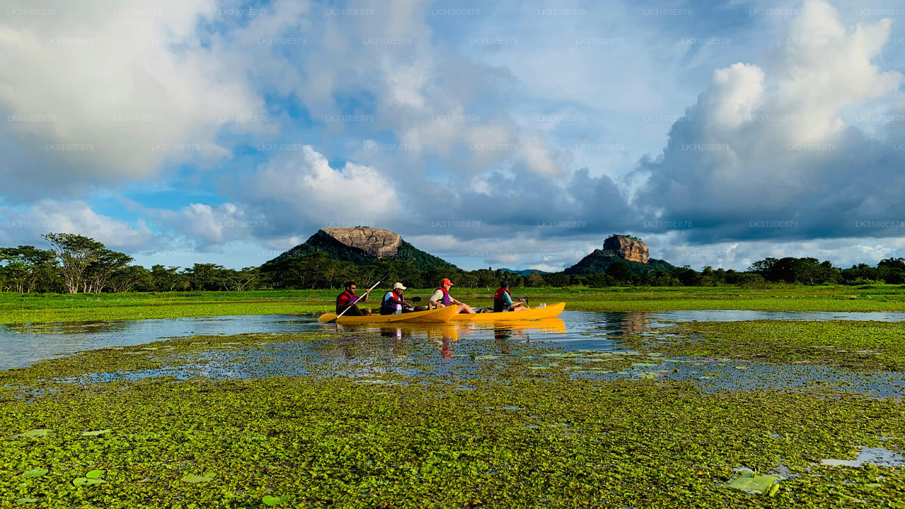 Four people in a yellow kayak on a calm body of water with greenery and mountains in the background.